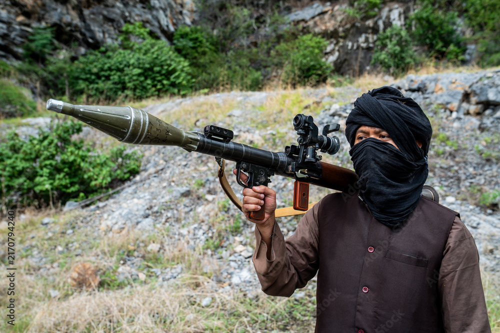 Naklejka premium Warrior holds a rocket launcher while standing in a rocky area surrounded by greenery