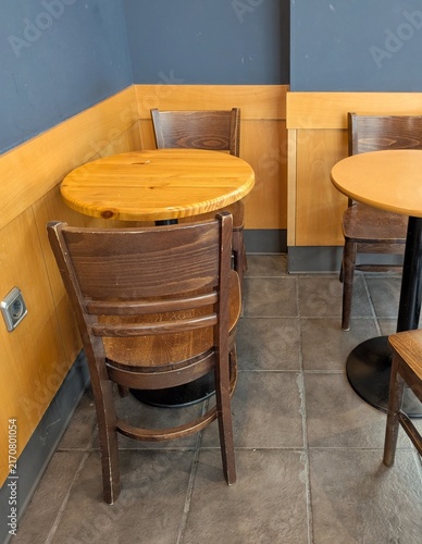 Vista de cerca de una mesa redonda con sillas sencillas de madera, en una cafetería, restaurante o comedor de hotel
