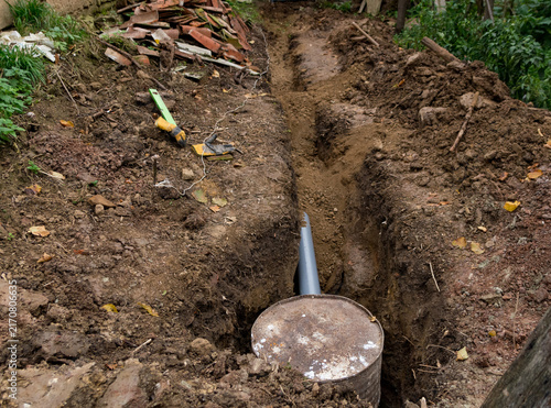 Backfilling a dirt trench over a PVC wastewater pipe and an improvised barrel septic tank

