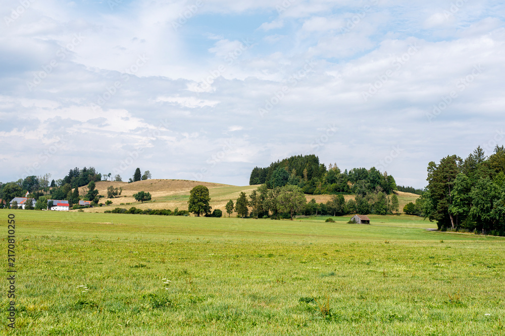 Naklejka premium Expansive rural landscape featuring green fields, rolling hills, forests, and a distant village.