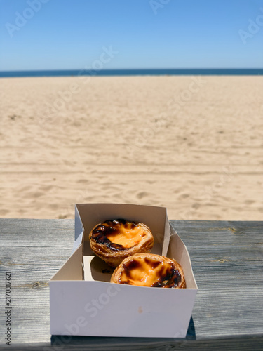 Portuguese custard tarts on beach bench with ocean view