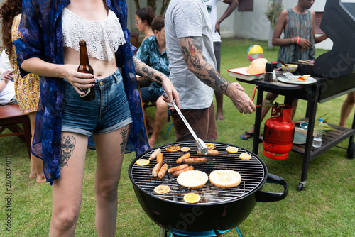 Young white woman and tattooed man grilling food at a backyard barbecue
