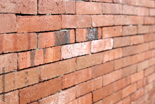 An angled close-up view of a rustic red brick wall showcasing detailed clay textures with a shallow depth of field fading into the background.