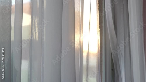 Warm evening sunlight shining through a sheer white curtain gently moving in the breeze, creating a peaceful and relaxing atmosphere inside a home.