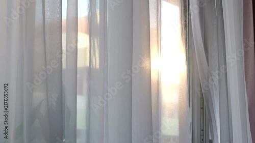 Warm evening sunlight shining through a sheer white curtain gently moving in the breeze, creating a peaceful and relaxing atmosphere inside a home.