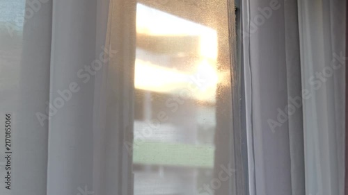 Soft golden evening sunlight glowing through a translucent white curtain moving gently in the breeze, creating a dreamy abstract interior background.