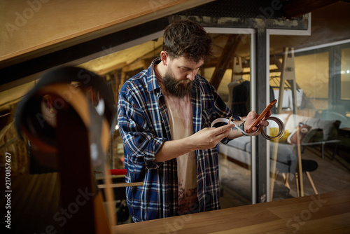 Cuadro en lienzo Young handyman checking replacement part against smartphone at garage workbench
