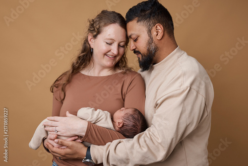 Loving Multiracial Parents Holding Newborn Baby Together in Warm Studio Family Portrait