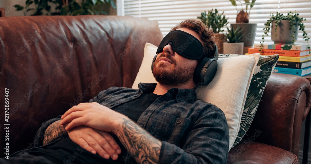 Fototapeta premium Man wearing eye mask and headphones resting and relaxing on a leather couch
