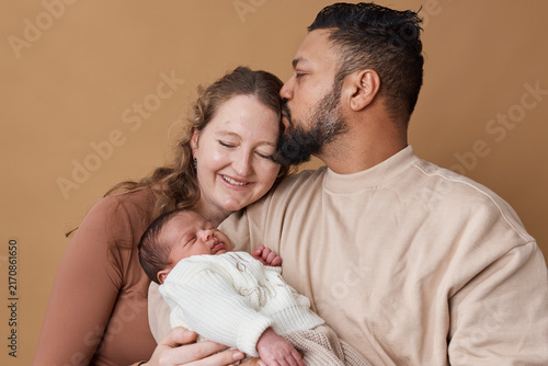 Multiracial Family With Newborn Baby - Loving Parents Embrace Infant in Warm Studio Portrait