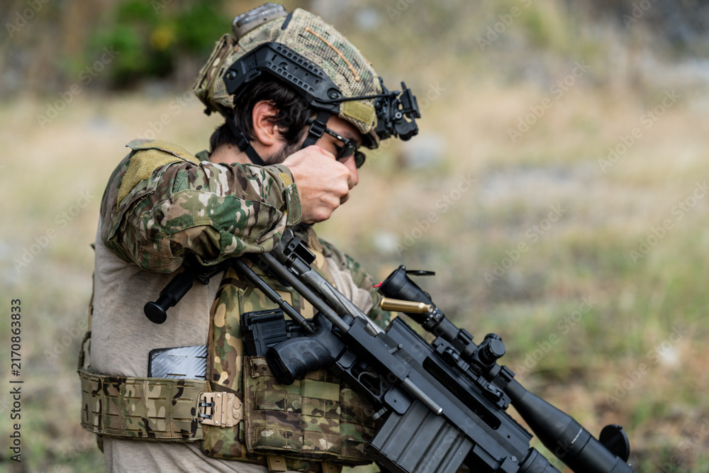Fototapeta premium Soldier prepares weapon at training site in outdoor setting during daytime hours