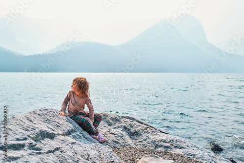 Boy sitting on a rock at a mountain lake looking at hazy peaks