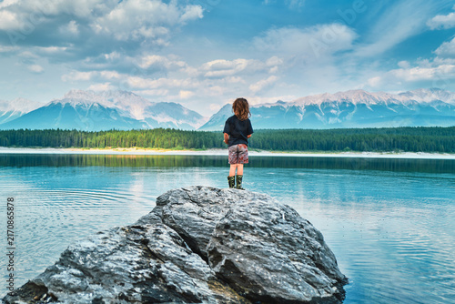 Boy standing on a rock facing a turquoise mountain lake from behind