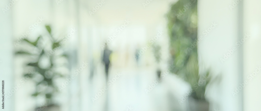 Obraz premium A softly focused image of a modern office hallway featuring greenery and people walking in a blurred background, conveying a sense of calm and professionalism.