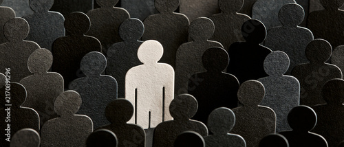 A prominent white human silhouette stands distinctly within a vast and textured crowd of dark gray and black abstract paper cutouts, powerfully symbolizing individuality, uniqueness, and