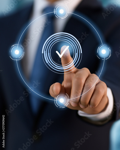Digital Verification Process: A businessman in a dark suit and tie touches a holographic interface, selecting a digital checkmark within a circular flow.
