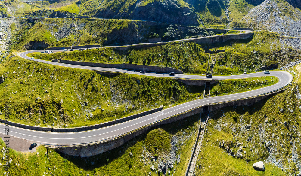 Obraz premium Curving Alpine Road Cutting Through Green Carpathian Mountains. Mountain Infrastructure and Serpentine Highway. A road with successive serpentines
