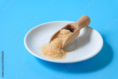 Konstfotografi Brown Cane sugar in wood scoop on white dish.