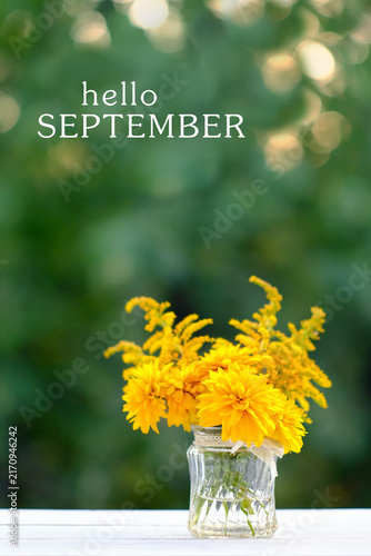 Hello september greeting card. beautiful composition with yellow flowers in glass vase close up on table in garden. rudbeckia laciniata (rudbeckia golden ball), symbol of summer end, autumn season.