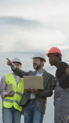 Diverse construction workers in hard hats and safety vests react with joy and excitement while looking at a laptop outdoors Suitable for teamwork, achievement and project success concepts.