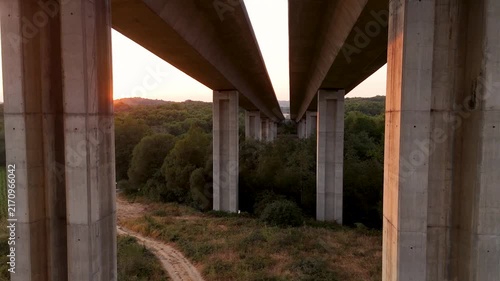 Concrete highway bridge pillars rising above green forest at sunset