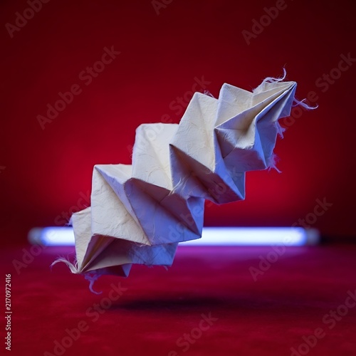 Complex folded geometric paper origami structure hovering above red surface with blue neon glow geometric art floating paper complex design