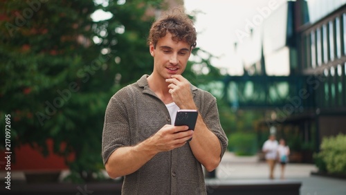 Foto Young man with curly hair looking at his smartphone outdoors in a city setting