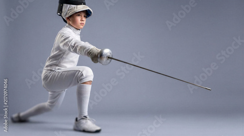 Young fencer executing lunge in competitive posture on gray background  