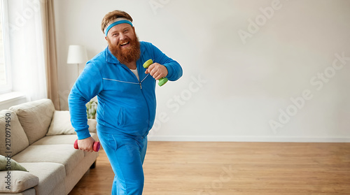 A humorous and fun-loving overweight with a red beard wearing sportswear and playfully exercising with dumbbells indoors. funny humorous playful fun loving overweight fat chubby large man male