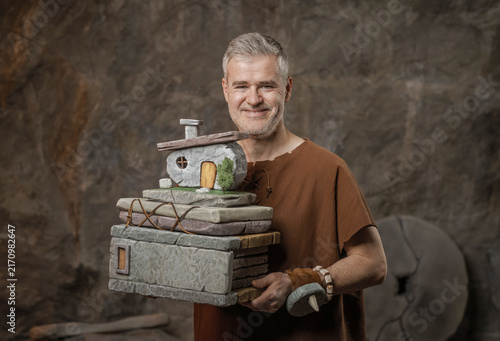 Obraz na płótnie Smiling Prehistoric Architect Carrying Stone House Model and Documents