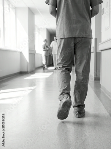 Monochrome nurse walking away with strong shadows across a tiled floor