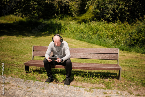 Принти на полотні Man listening music headphones, using smartphone on park bench