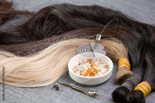 Natural human hair extensions prepared for hot fusion keratin bonding. Keratin tips, hair extension tools and clips arranged on a salon workstation, professional hair extension application