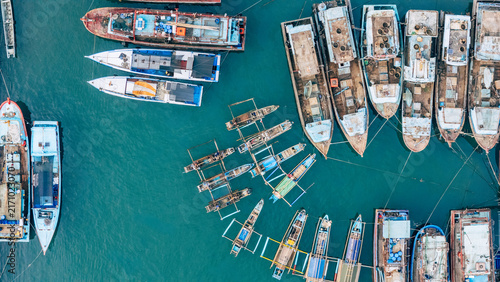 Aerial view of numerous fishing boats moored in the turquoise harbor waters, showcasing traditional outrigger designs and wooden hulls Palabuhanratu, West Java, Indonesia.
