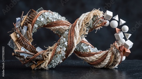 Conceptual infinity symbol created from recycled copper wire, rope, and crushed glass with floating geometric shapes, perfect for circular economy and sustainability themes.