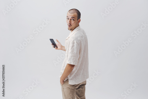 Surprised Young Man Holding Smartphone Looking Back Over Shoulder