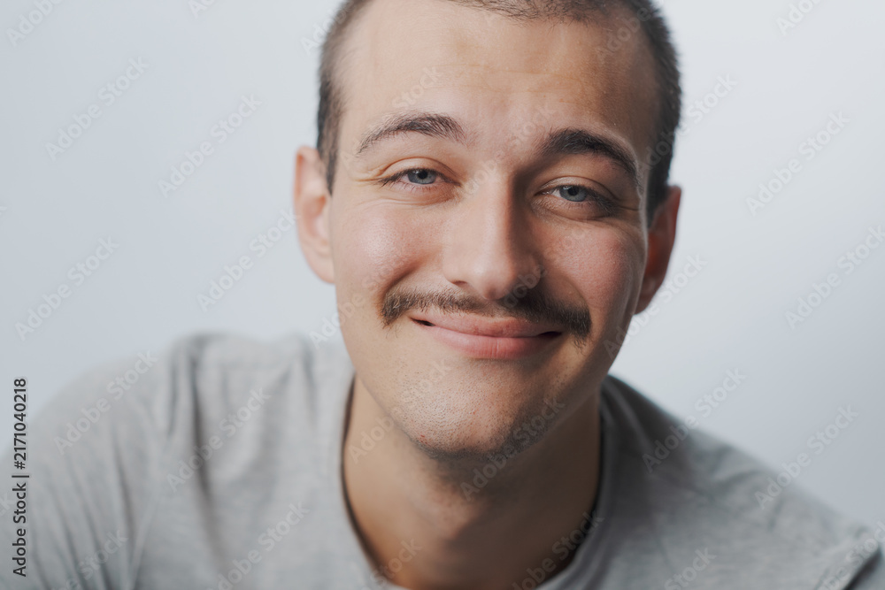 Naklejka premium Close-up portrait of a young man with mustache smiling softly at camera