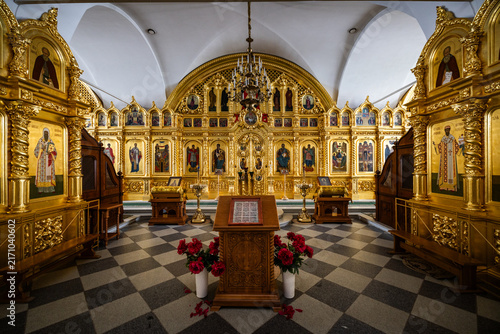 View of the ornate golden iconostasis and wooden lectern inside the church at Solovetsky Monastery, with a checkered floor and red peonies in Solovetsky, Arkhangelsk Oblast, Russia.