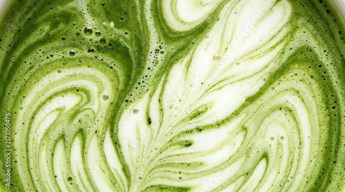 Macro close up of creamy matcha green tea latte with swirling milk foam, bubbles and marbled texture creating an abstract organic beverage background.