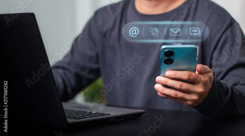 Business professional using smartphone beside laptop with digital communication icons, representing mobile service, customer support, online business, connectivity, marketing and technology.