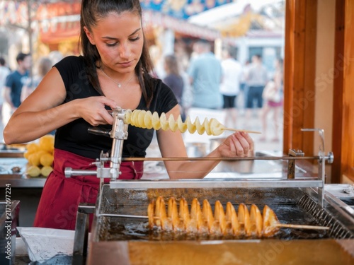 Spiralkartoffel am Spieß – Verkäuferin schneidet eine Kartoffelspirale und bereitet sie im heißen Fett zu. Beliebtes Street Food auf dem Volksfest mit frischer Zubereitung.