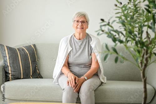 Portrait of elderly woman over grey background sit on sofa