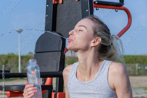 Fotografie Young woman spitting water stream near fitness equipment outdoor workout