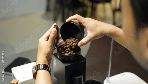 Принти на полотні Close-up of a barista pouring freshly roasted coffee beans into an electric coffee grinder, showcasing the preparation process in a modern specialty coffee shop