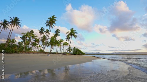 Close-up view of blue wave on tropical palm beach of Indian Ocean. Sea waves on golden sand. Palm trees against the dawn sky. Waves crash onto the sandy beach. Changeable windy weather.