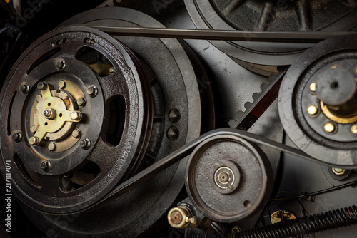 Close-up of industrial belt drive mechanism with steel pulleys and tensioner roller on agricultural machinery.