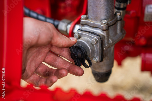 Mechanic hand opening protective plastic cap on hydraulic or pneumatic valve system of red agricultural tractor.