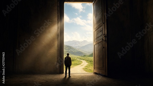 Person standing in open doorway looking at mountain landscape with bright sunlight rays