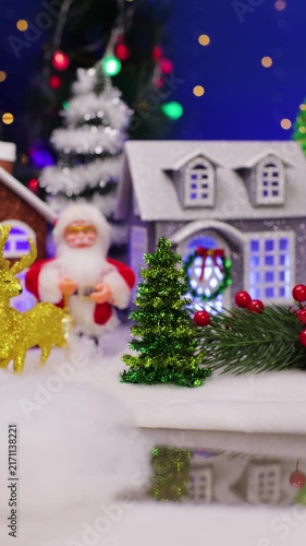 Close-up of a little funny Santa Claus jumping in front of a beautiful Christmas village