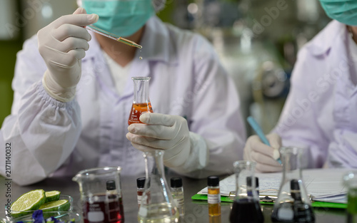 Scientists wearing masks and gloves conduct chemical experiments with liquids in a laboratory, using droppers and recording observations.